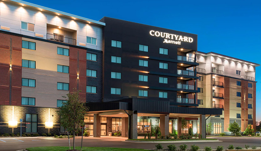 Exterior of the Courtyard by Marriott hotel in Mount Pleasant, Michigan, illuminated at dusk, with its entrance, balconies, and Marriott signage visible.