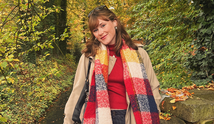 Shannon Fitzgerald wears a colorful scarf and tan jacket as she poses in a forest.