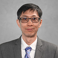 Keejae Hong in a professional headshot, wearing glasses, a gray suit, and a striped tie against a neutral background.
