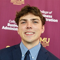 Koby Rhymer smiling in a professional headshot, wearing a suit and tie with a CMU backdrop.