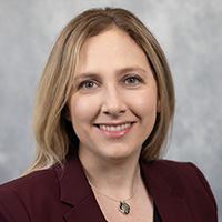 Lauren Zettel smiling in a professional headshot, wearing a maroon blazer against a neutral background.