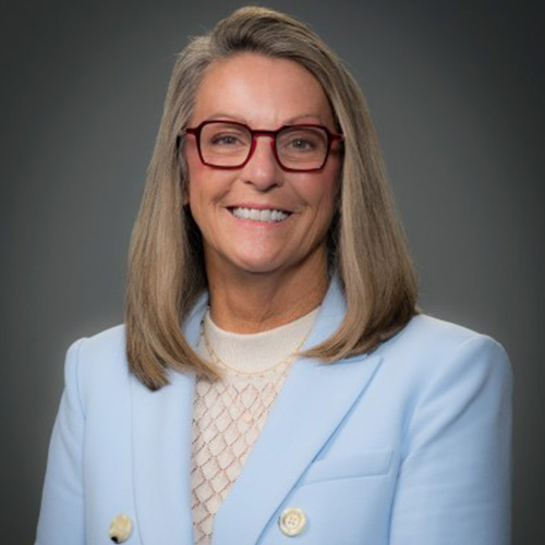 Melanie Kalmar wearing glasses and a light blue blazer, smiling in a professional portrait