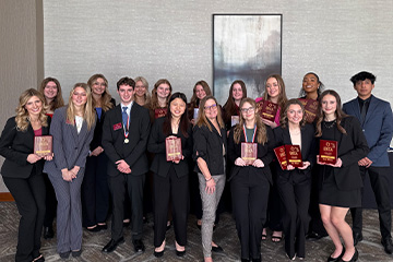 Sixteen CMU DECA competitors pose with their coach Shelly Bartosek at the DECA competition where they were finalists and finishers in many categories. They are all dressed in business professional clothing.