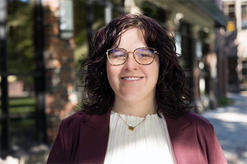 April Northrop smiles for an outdoor portrait, wearing glasses, a burgundy blazer and a white blouse.