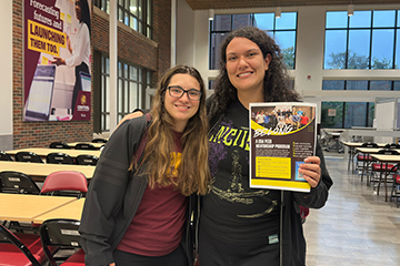 Jade Walleman (left) stands with another student holding a BELONG Peer Mentorship Program flyer inside Grawn Hall at Central Michigan University.