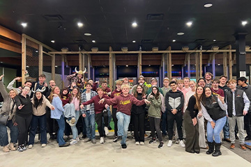 A large crowd of Business Residential College students strike silly poses at Valhalla Axe Throwing. They are smiling, some wear Viking horn helmets, and all look like they are having a great time.