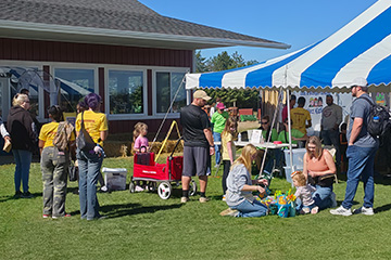 Business Residential College students and community members gather at the 37th annual Zonta Apple Fest in Mount Pleasant. Volunteers in yellow BRC shirts assist visitors near a blue-and-white tent while families enjoy children's activities on the lawn.