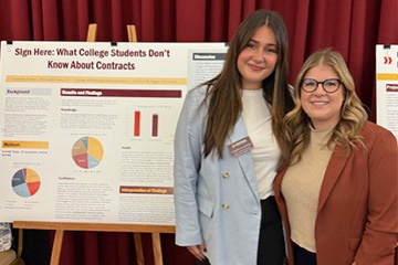 Carmella Cortez stands with her advisor, Jill Lauderman, in front of a poster displaying Carmella’s honors research. Carmella has long brown hair and wears a white shirt and light blue blazer; Jill has long blond hair and wears a burnt orange blazer.