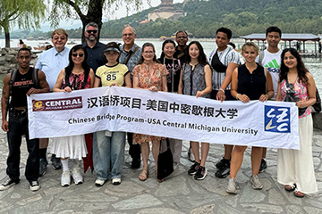 Students and faculty rom the CBA stand with Chinese counterparts from the Zhejiang University of Technology. They hold a banner tin Chinese and English that reads Chinese Bridge Program-USA Central Michigan University. Behind them is a river and temple.