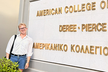 Ethan Rauschert stands beside a sign for Deree – The American College of Greece, where he studied abroad for a semester.