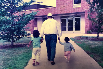 Lee Curtis walks hand in hand with two young children along a sidewalk toward Grawn Hall at Central Michigan University.