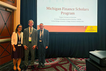 Claudine Salgado, Luke West, and Brad Taylor stand beside their Michigan Finance Scholars presentation at AAA Global Connect.