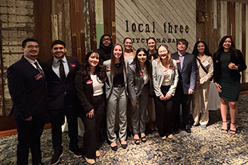 Twelve Queller Scholars dressed in business professional clothing stand in front of the Local Three restaurant in Atlanta.