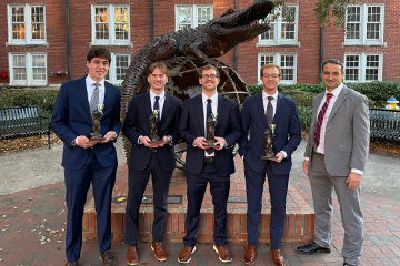 Ethan Schweitzer, Wyatt Ross, Trevor Carnovsky, and Adam Rose stand with a classmate in front of a Florida Gator statue at the University of Florida Stock Pitch Competition. They hold trophies from their second place finish.