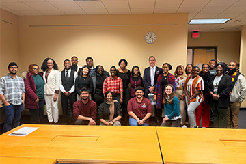 A group of Central Michigan University students, faculty, and staff pose together in a library conference room during a Toastmasters meeting, highlighting student participation and community.