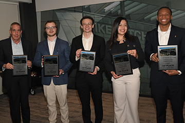Faculty member Brad Taylor and students Derek Ballas, Blake Jimenez, Carolina Hernandez Ruiz and Mark-Allen Gay stand together with first place plaques from the Wayne State Venture Capital competition. They are wearing business professional clothing.