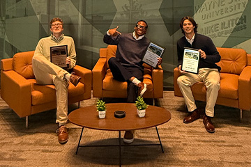 CMU students Caleb Baron, Mark-Allen Gay Jr. and Ryan Karwowski sit together holding their first-place awards from Wayne State University's Venture Capital Case Competition.