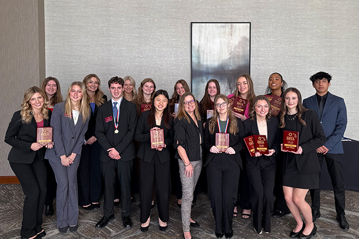 Sixteen CMU DECA competitors pose with their coach Shelly Bartosek at the DECA competition where they were finalists and finishers in many categories. They are all dressed in business professional clothing.