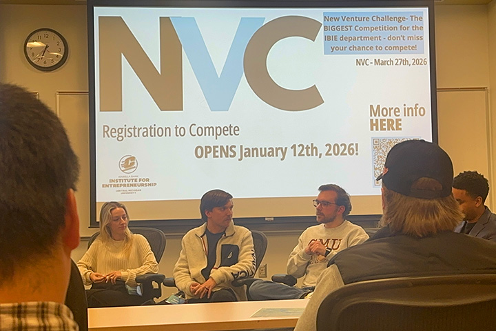 NVC 2026 mentors sit in chairs at the front of the Grawn 150G classroom. They are speaking to students about mentoring and entrepreneurship. Behind them is a display slide with details on the competition.