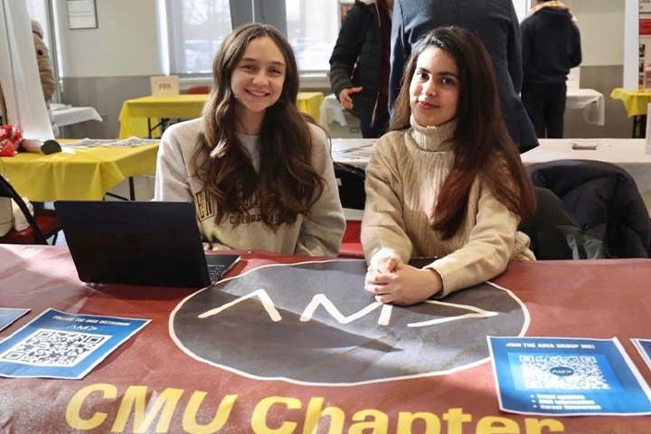 Sarah Firchau, left, and Aimen Khan sit behind a CMU American Marketing Association table during a student outreach event.