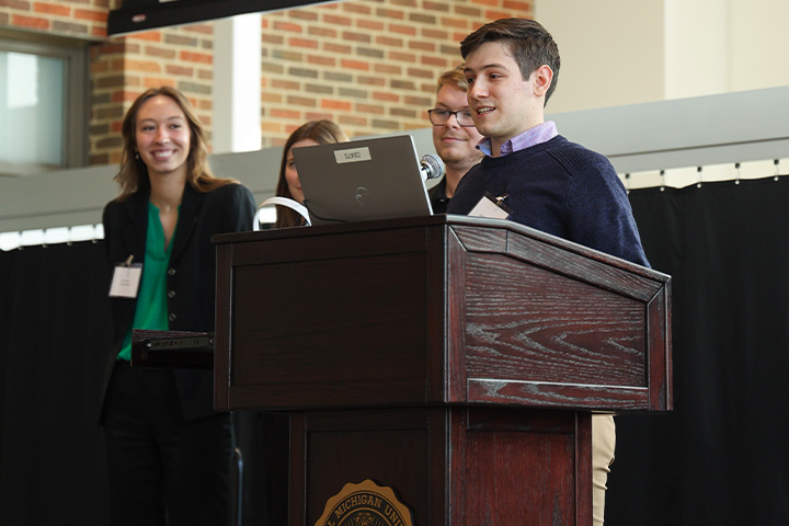 Student team presents at a podium during Boss Games while teammates stand behind, participating in a business competition.