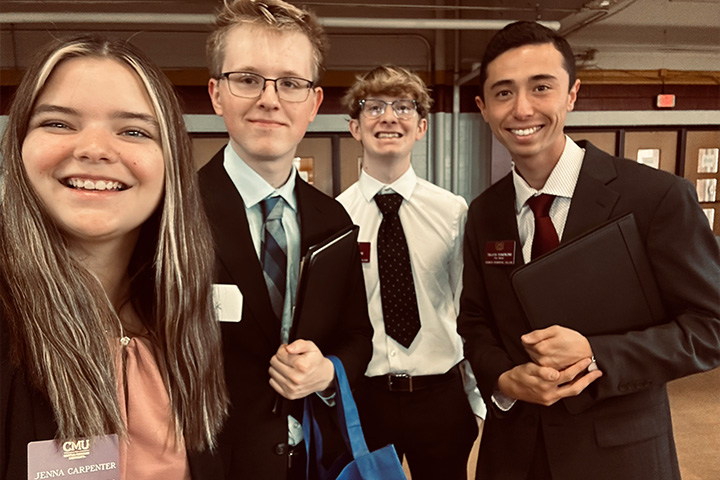 Jenna Carpenter-Ferguson (left) and Travis Tompkins (right) stand with peers from the Business Residential College. They are all in business professional clothing and pose for a selfie.