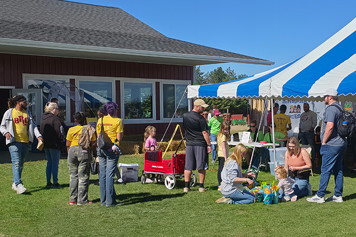 Business Residential College students and community members gather at the 37th annual Zonta Apple Fest in Mount Pleasant. Volunteers in yellow BRC shirts assist visitors near a blue-and-white tent while families enjoy children's activities on the lawn.