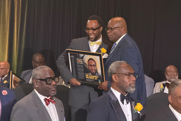 Management faculty member Cleamon Moorer Jr. accepts a 2026 Michigan Chronicle Men of Excellence award while holding a framed recognition plaque during the awards ceremony.