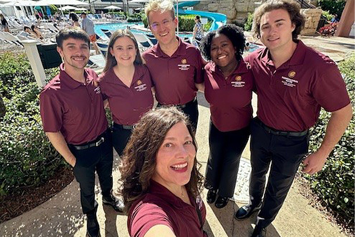 Concha Allen takes a selfie with students on a trip. They are all wearing maroon polo shirts with embroidered CMU logos with black pants.