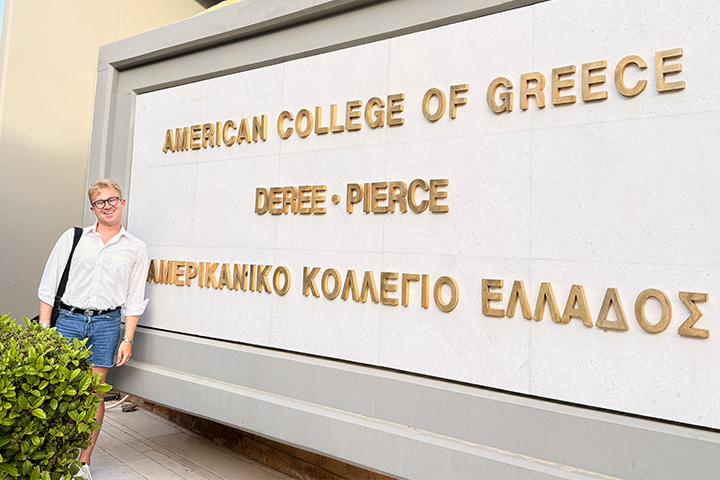 Ethan Rauschert stands beside a sign for Deree – The American College of Greece, where he studied abroad for a semester.