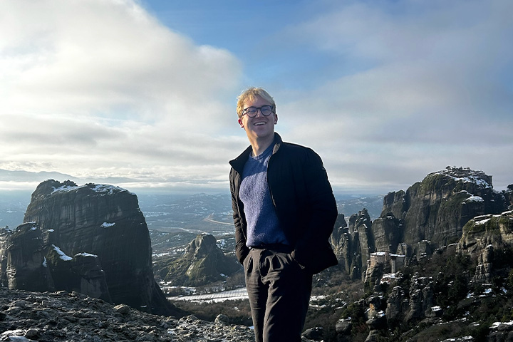 Ethan Rauschert stands among towering rock formations overlooking the mountainous landscape of Meteora, Greece.