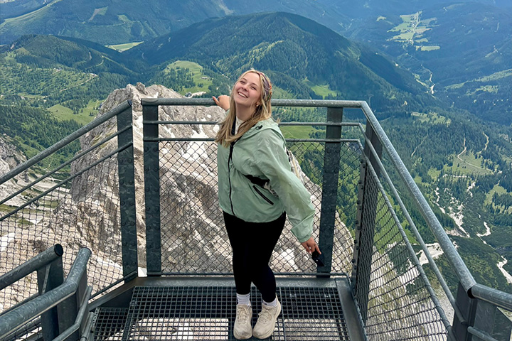 Kaitlyn Klumpp smiles on a mountain observation platform overlooking a forested alpine valley.