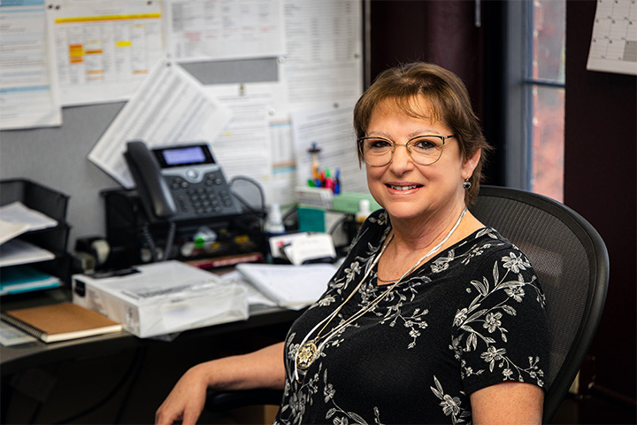 Melissa Davidson, administrative office assistant in CMU's Department of Economics, smiles while seated at her desk in Grawn Hall.