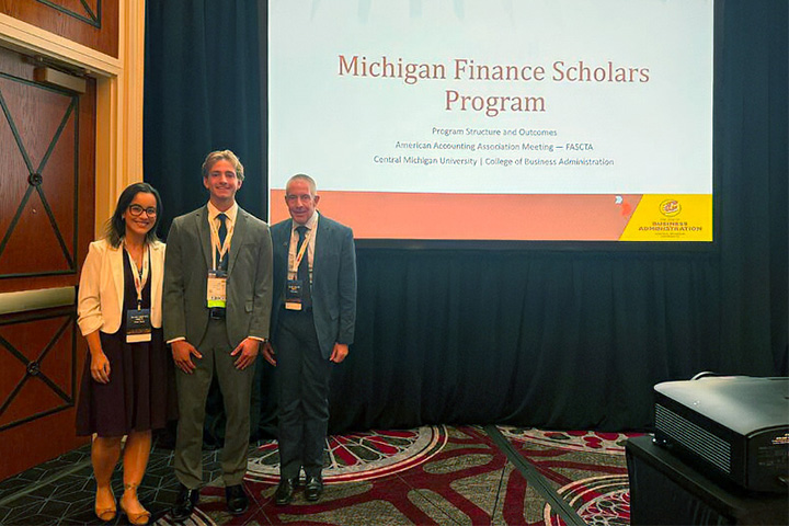 Claudine Salgado, Luke West, and Brad Taylor stand beside their Michigan Finance Scholars presentation at AAA Global Connect.