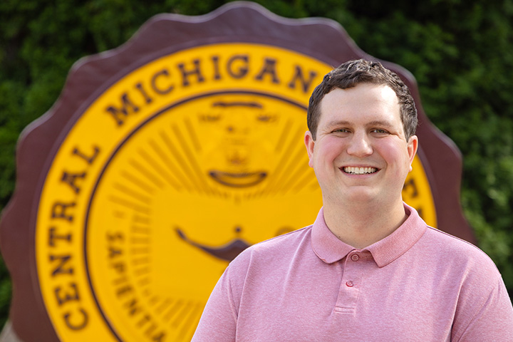 Nathan Blizzard smiles in front of the Central Michigan University seal.