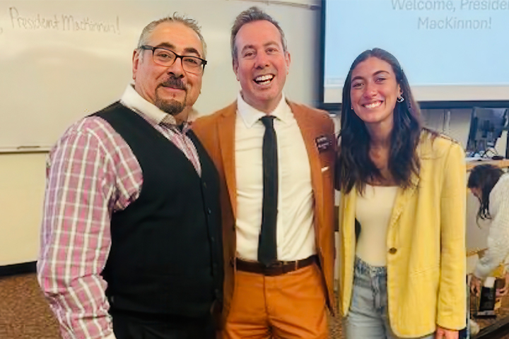 President Neil MacKinnon stands with faculty member Nick Hussein and a hospitality student in a classroom where MacKinnon gave a guest lecture. They are all smiling at the camera and behind them 