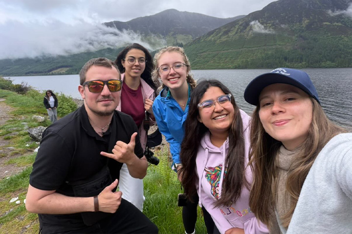 Reghan Haley joins fellow travelers for a lakeside group photo, with green mountains and low clouds behind them.