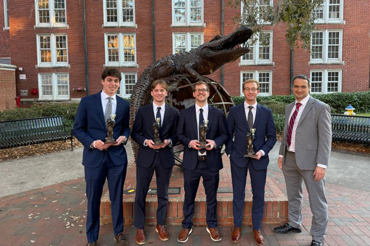 Ethan Schweitzer, Wyatt Ross, Trevor Carnovsky, and Adam Rose stand with a classmate in front of a Florida Gator statue at the University of Florida Stock Pitch Competition. They hold trophies from their second place finish.