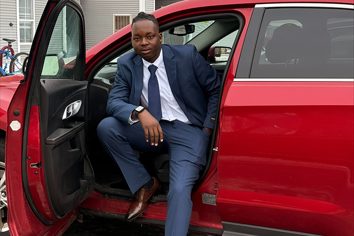 Tamuka Kanyai in a navy suit steps out of a red car, dressed professionally.