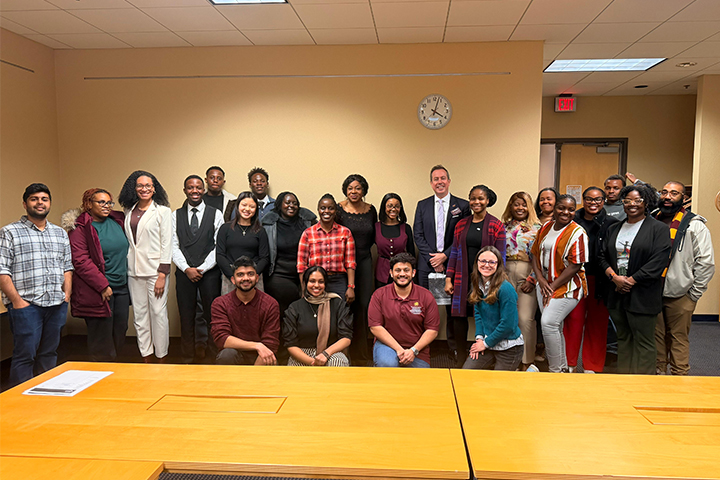 A group of Central Michigan University students, faculty, and staff pose together in a library conference room during a Toastmasters meeting, highlighting student participation and community.