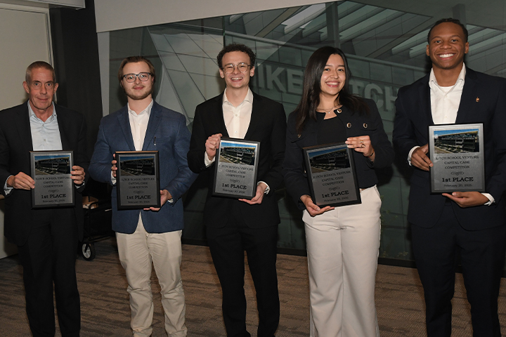 Faculty member Brad Taylor and students Derek Ballas, Blake Jimenez, Carolina Hernandez Ruiz and Mark-Allen Gay stand together with first place plaques from the Wayne State Venture Capital competition. They are wearing business professional clothing.