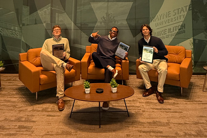 CMU students Caleb Baron, Mark-Allen Gay Jr. and Ryan Karwowski sit together holding their first-place awards from Wayne State University's Venture Capital Case Competition.