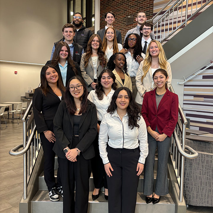 Queller Leadership Scholars pose together in new business clothes on a staircase inside the College of Business Administration.