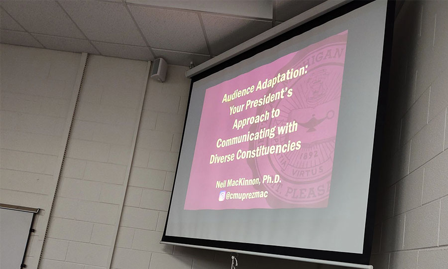 900x600_Article_Inset_Advanced_Selling A PowerPoint slide appears on a pull-down screen in the corner of a classroom. The slide reads: Audience Adaptation: Your President's Approach to Communicating with Diverse Constituencies Neil MacKinnon, Ph.D. @cmuprezmac.