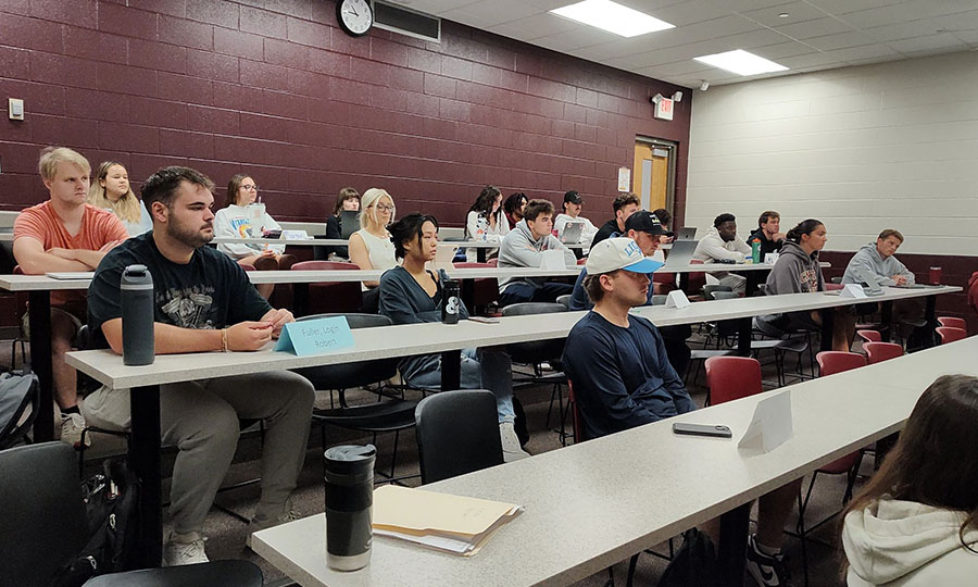 900x600_Article_Inset_Advanced_Selling2 A group of twenty students sit at long tables in a CMU classroom. The students are facing forward and focused on the front of the classroom, which isn't visible in the image. The back wall of the class is painted maroon and the other side is white.