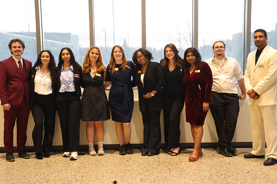 Kaye Reimers wears a black dress and stands in the center of a group of nine students at the 2025 NVC event in the Bio Sciences building.