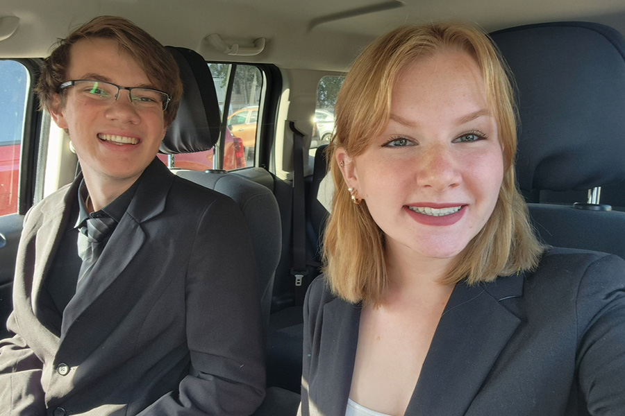 Colten Lambart, left, and Cailin Lambart, right, pose for a selfie together in a car with a dark interior. Colten has a coordinating dark gray jacket, shirt and tie. Cailin wears a dark gray jacket over a white shirt.
