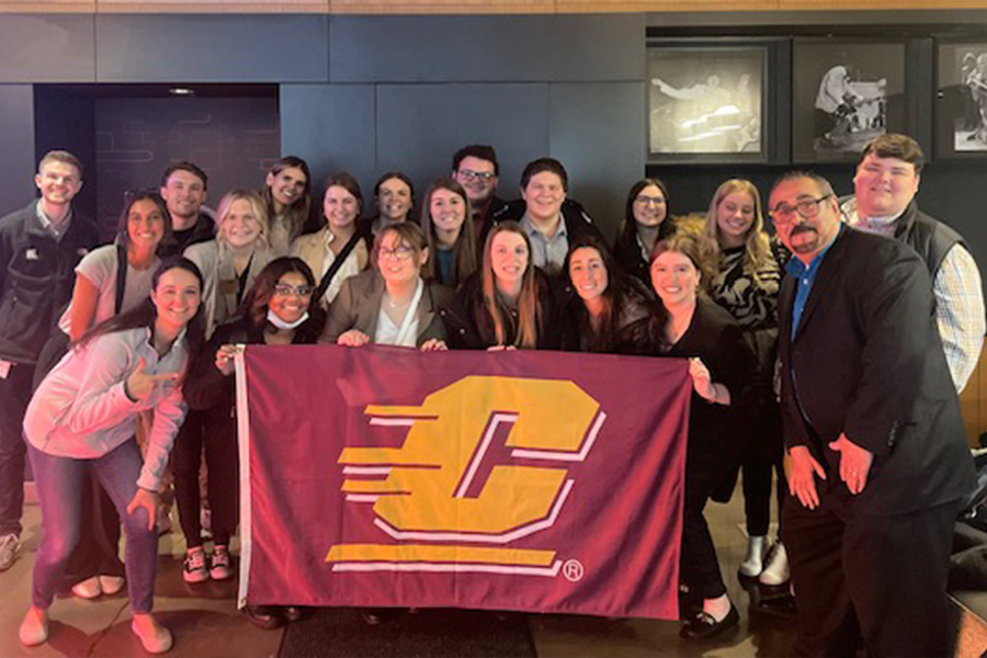 A group of hospitality students and faculty member Nick Hussein pose with a CMU Action C flag.