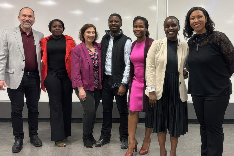 Yaw Owusu Adarkwah wears black pants, a white button down and black vest and stands with a 6 Toastmasters members.