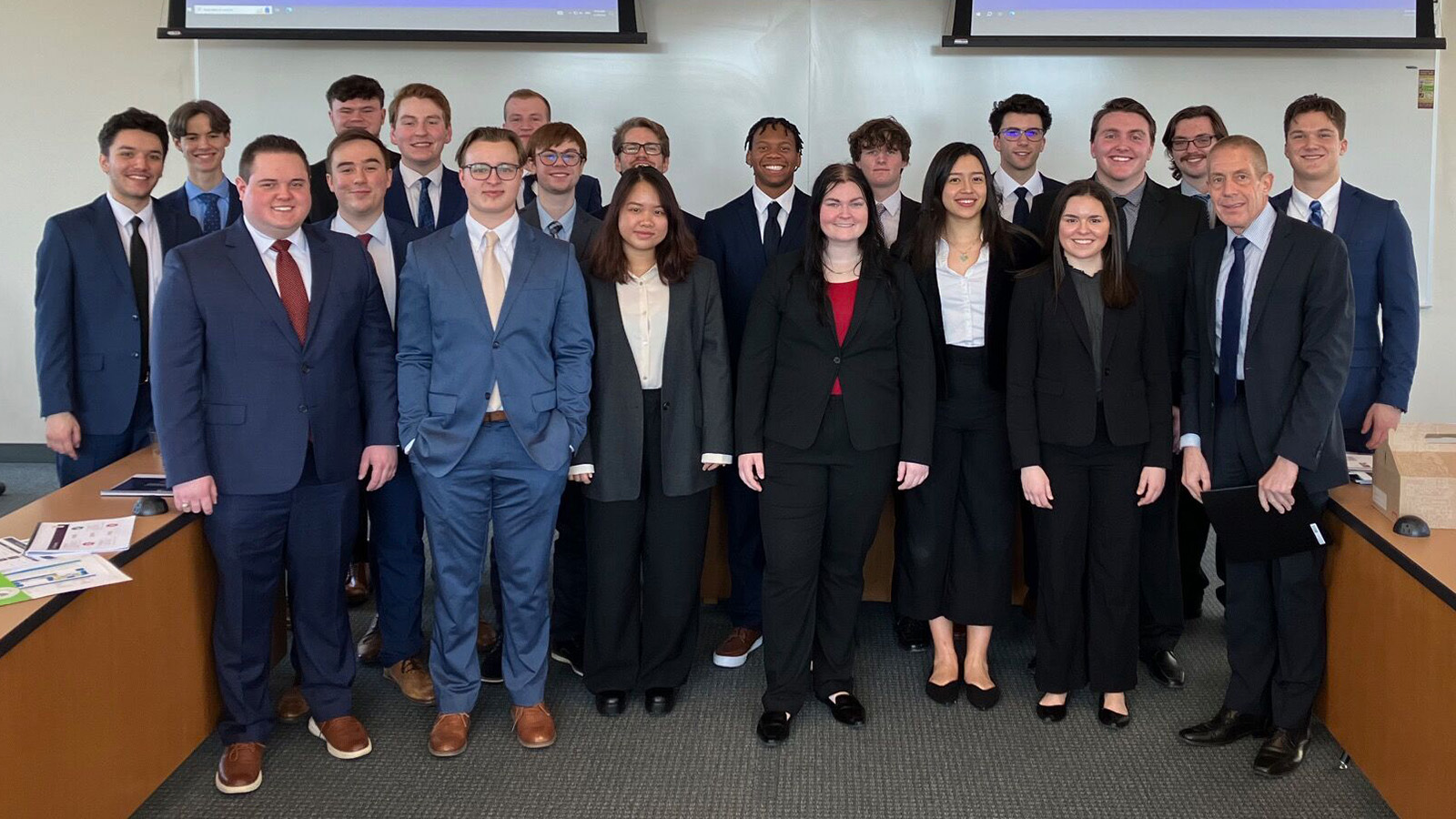 A picture of the five teams from CMU competed in the 2024 ACG Cup in Grand Rapids. They are professionally dressed and standing as a group in a boardroom.